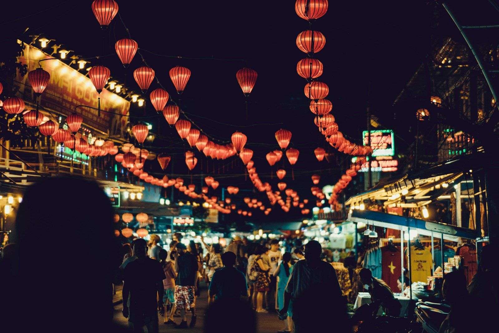 Food stalls lit by hanging lanterns at a night market, like Phuket's evening markets in July