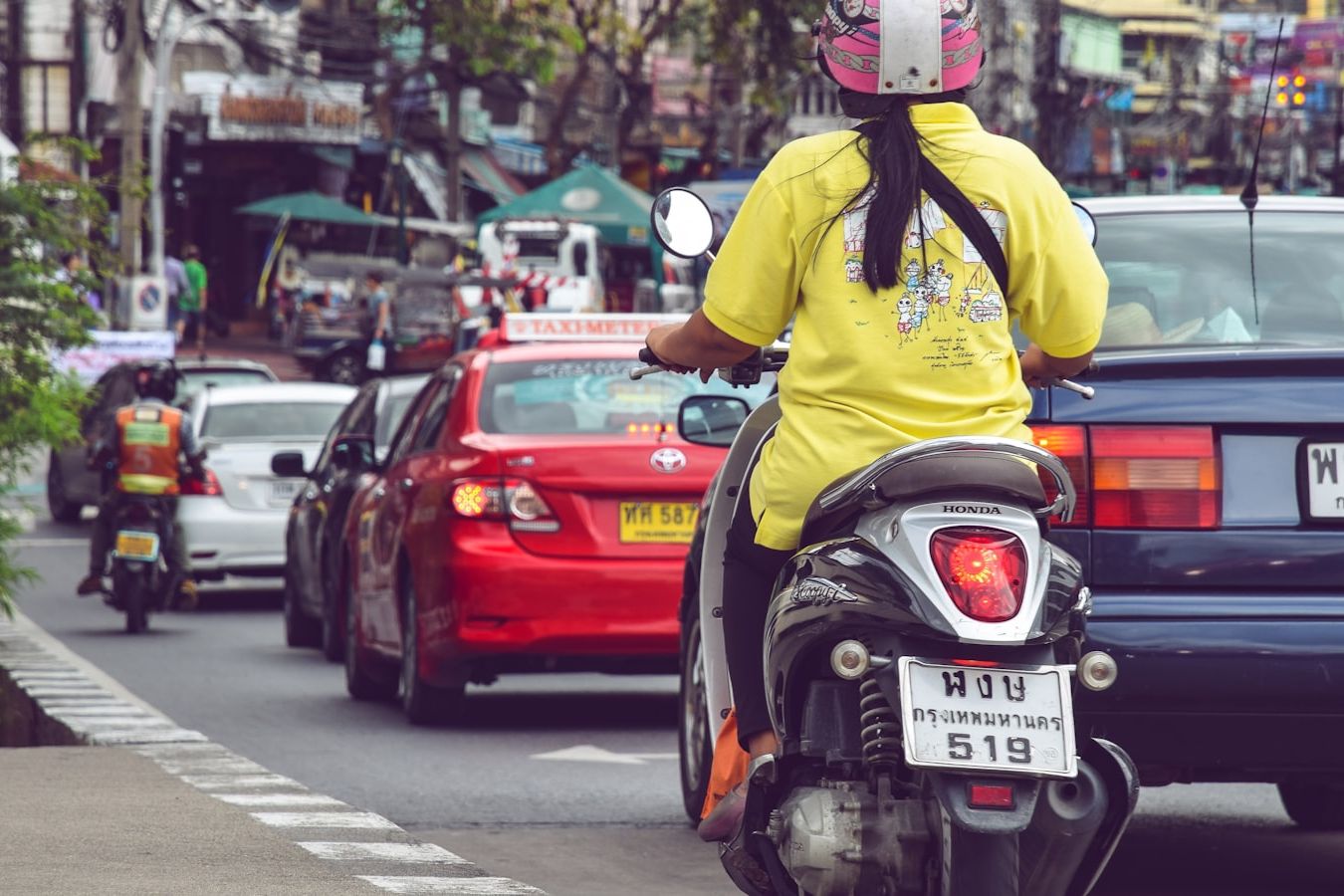 A rider on a scooter in Thailand, helmet on, riding on the left