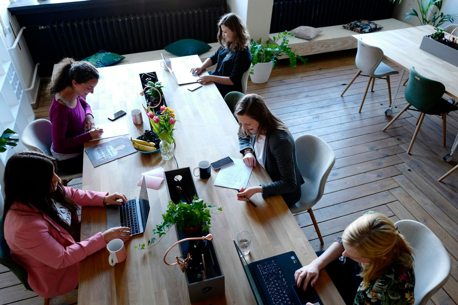 Remote workers at a shared table in a bright, plant-filled coworking space