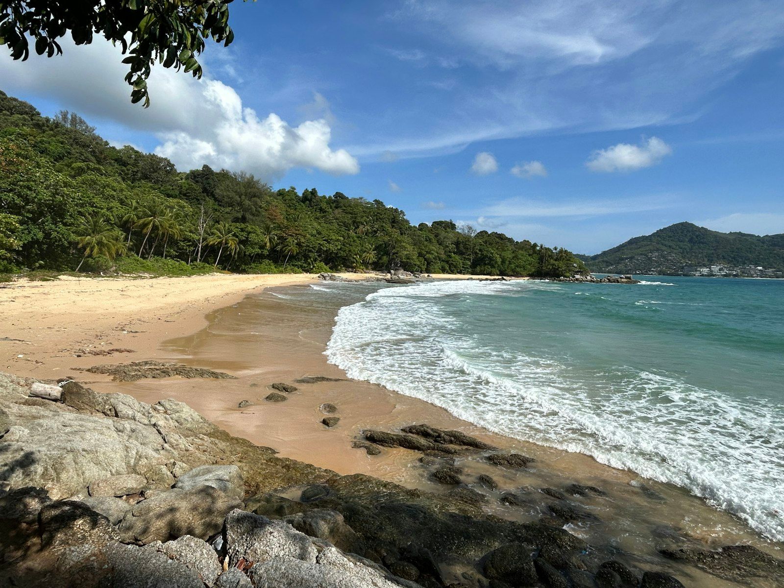 A quiet Phuket beach beside a lush green hillside during the July green season