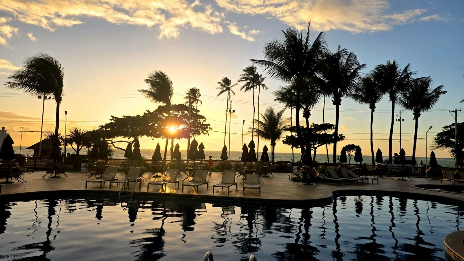 Golden sunset over a Phuket beach club pool with silhouetted palm trees