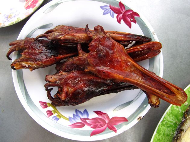 Grilled duck beaks glazed dark red on a floral plate, a nose-to-tail Thai snack