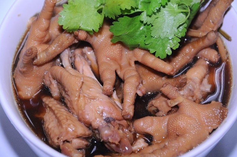 A bowl of braised Thai chicken feet in dark soy broth topped with fresh coriander