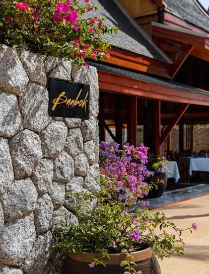 Buabok entrance sign on a stone wall with bougainvillea at the Thai restaurant inside Amanpuri, Bang Tao, Phuket