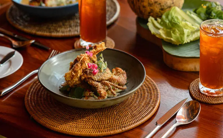 Crispy soft-shell crab dish with iced tea on a wooden table at Buabok, a Thai restaurant in Bang Tao, Phuket