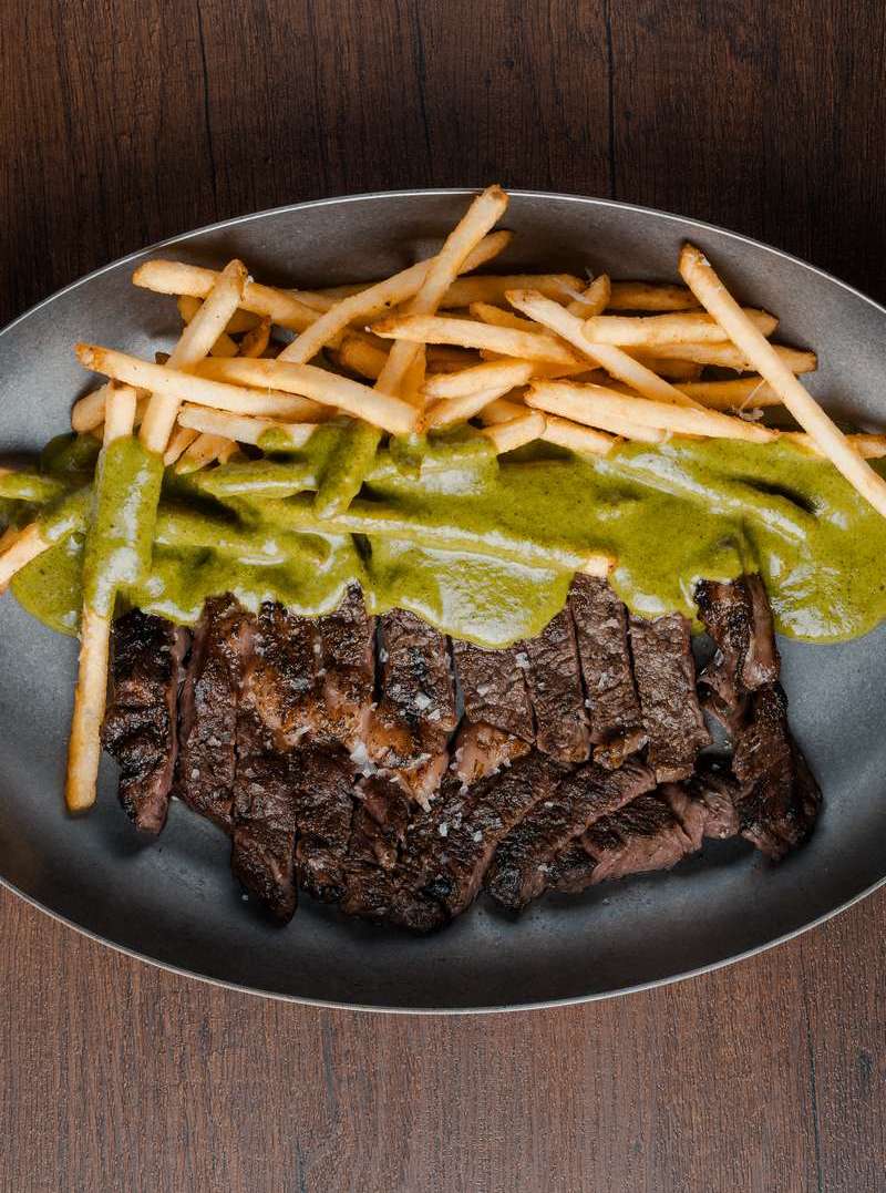 Sliced grilled steak with fries and green chimichurri sauce on a metal plate at Five Olives, Bang Tao Phuket