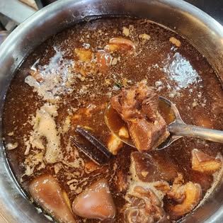 Metal pot of dark braised pork broth with meat pieces and a spoon at Go Ang Seafood restaurant, Old Town Phuket