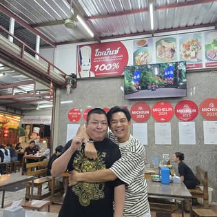 Two smiling men posing under MICHELIN plaques inside Go Benz pork noodle restaurant, Old Town Phuket