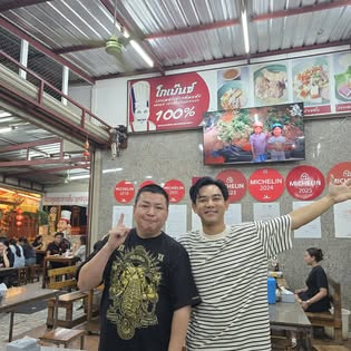 Two men giving peace signs beside MICHELIN plaques inside Go Benz Asian noodle restaurant, Old Town Phuket