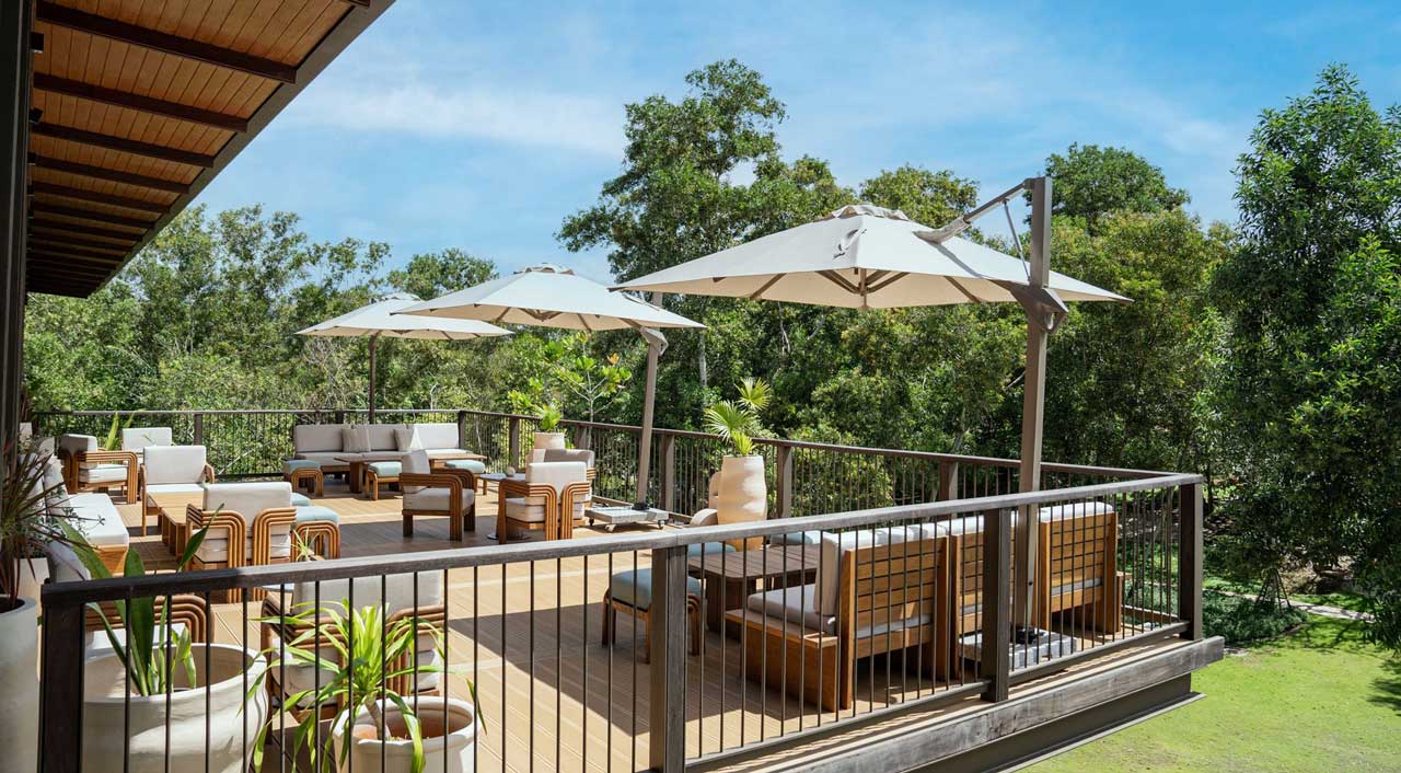 Outdoor deck terrace with lounge seating and parasols overlooking greenery at Jampa farm-to-table restaurant in Bang Tao, Phuket