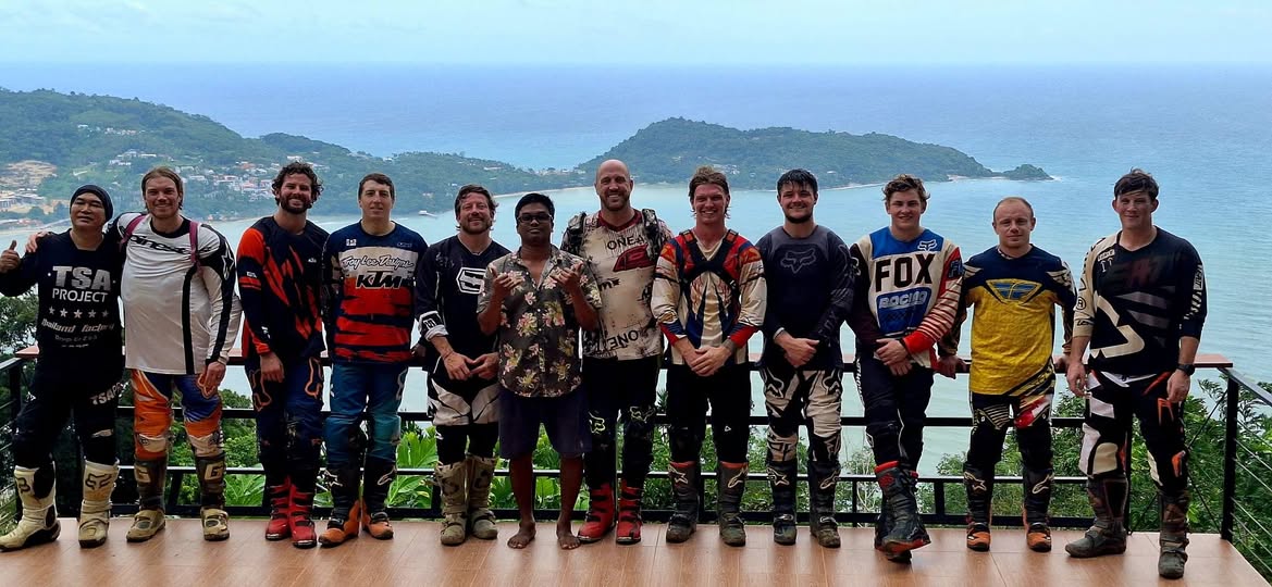 Group of enduro motocross riders posing at a coastal viewpoint deck on the JunJaow Trail above Patong, Phuket