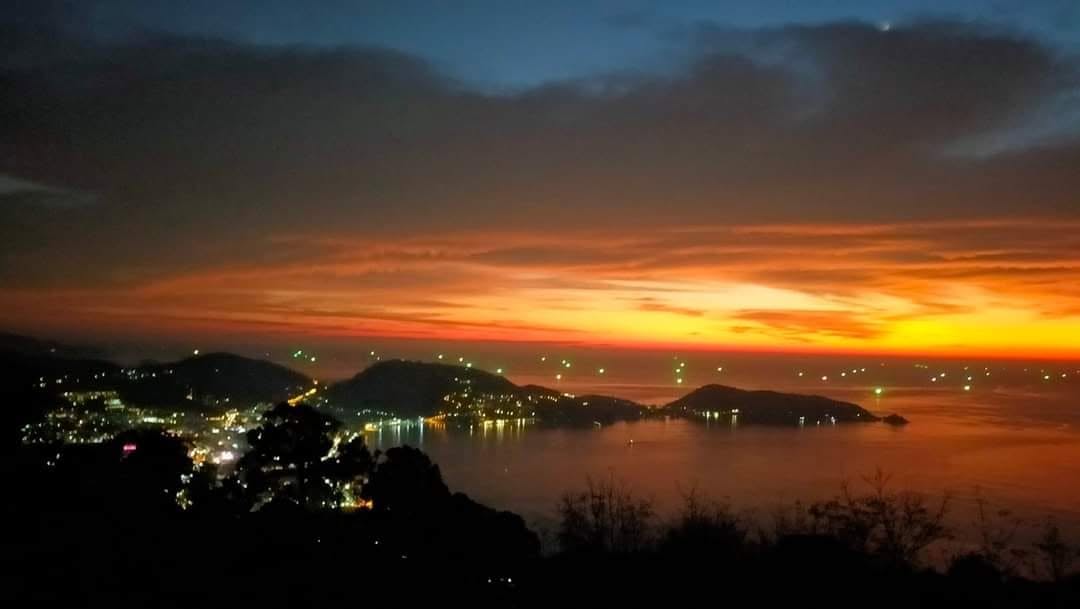 Fiery sunset over Patong bay city lights seen from the hilltop viewpoint at JunJaow camping cafe above Patong, Phuket