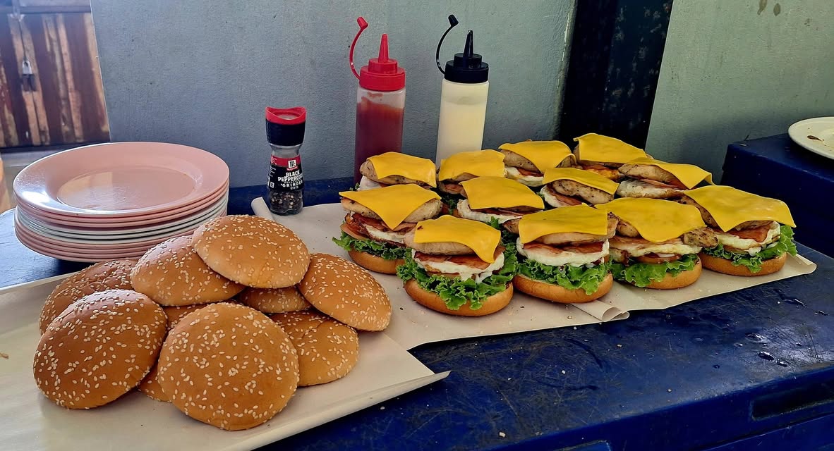 Sesame buns, cheese and sauce bottles beside grilled burgers being assembled at JunJaow camping cafe above Patong, Phuket