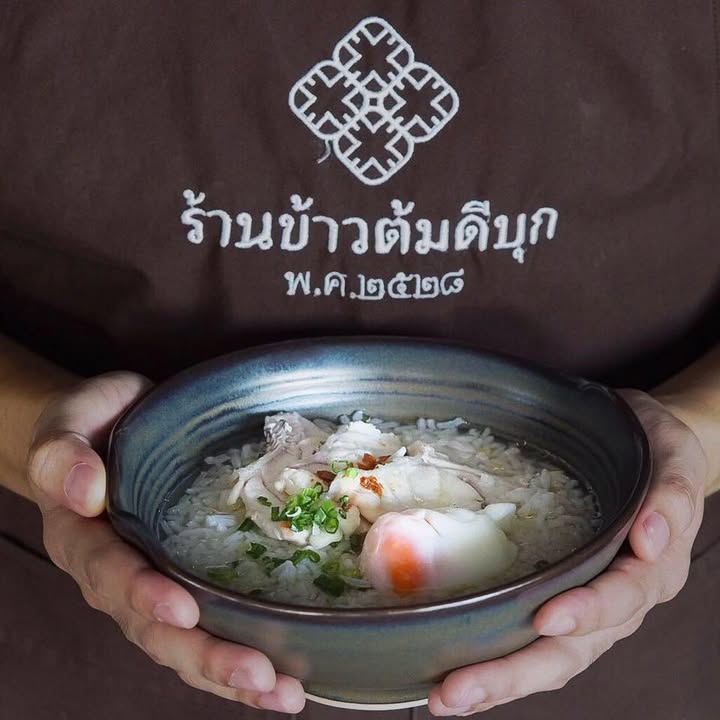 Hands holding a bowl of khao tom rice porridge with chicken and soft egg at Khao Tom Dibuk in Phuket Old Town