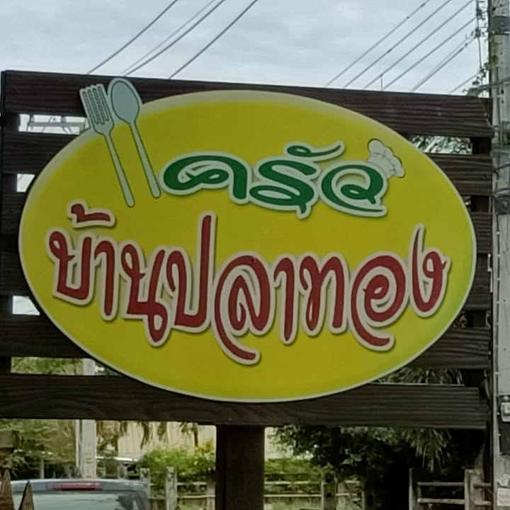 Bright yellow oval signboard with Thai lettering, fork, spoon and chef hat icons for Krua Baan Platong in Bang Tao, Phuket
