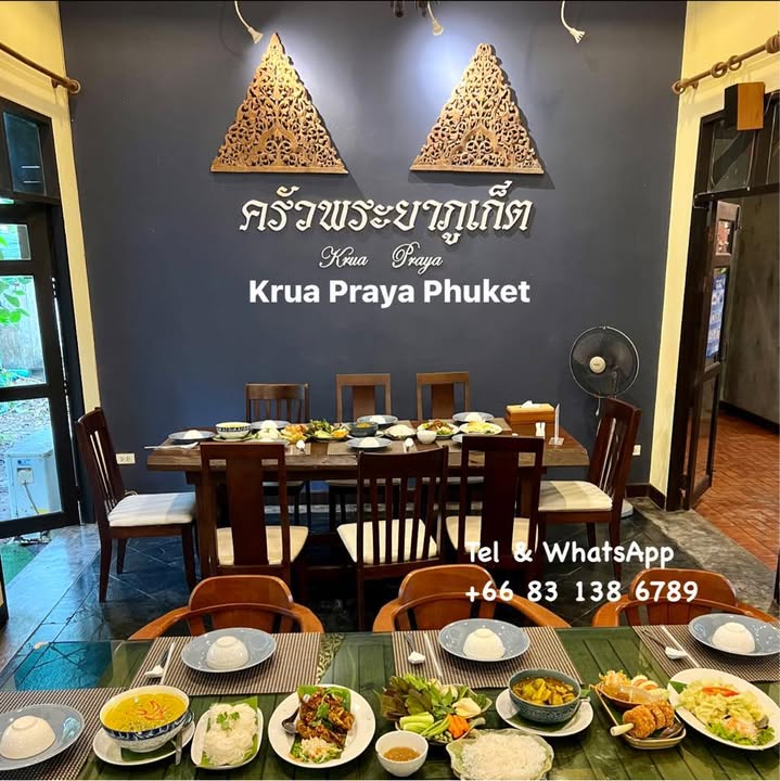Wooden tables set with a spread of Southern Thai dishes below the Krua Praya Phuket sign at this restaurant in Bang Tao, Phuket