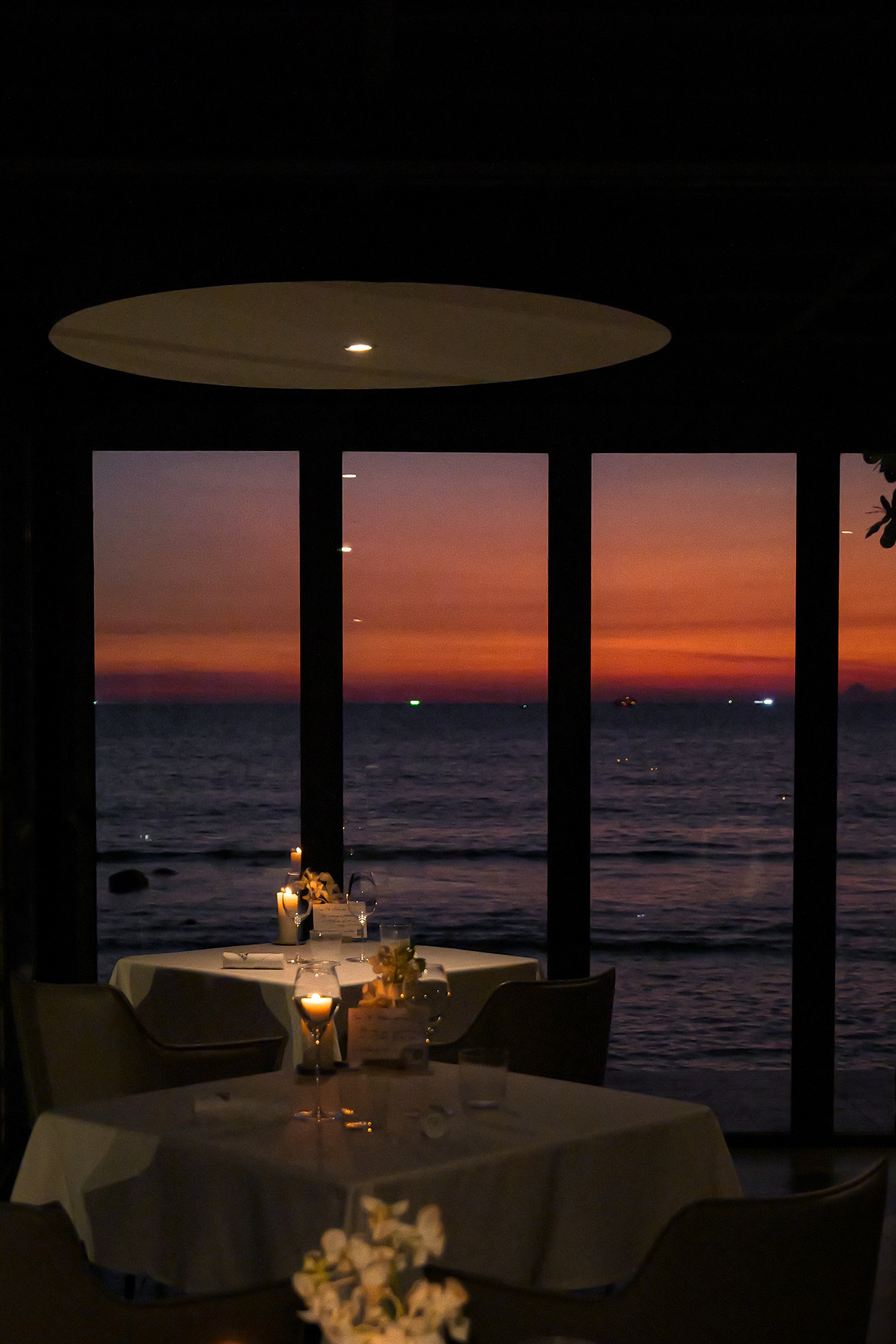 Candlelit dining tables framed by an orange and purple twilight sky over the sea at L'Arôme by the Sea in Patong, Phuket