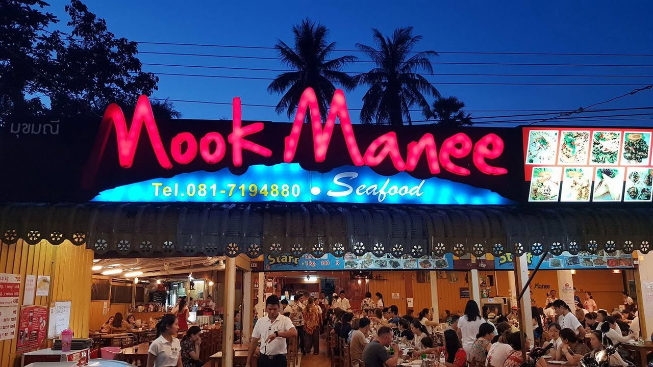 Neon Mook Manee Seafood sign glowing over busy diners at dusk, seafood restaurant near Rawai Beach, Phuket