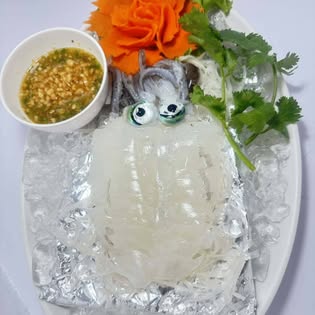 Fresh raw squid plated on ice with chili-garlic dipping sauce and carved carrot at Mook Manee seafood restaurant near Rawai Beach, Phuket