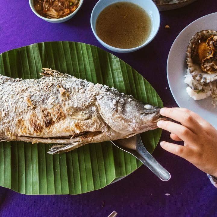 Whole salt-grilled fish on a banana leaf with dipping sauces and shellfish at Mor Mu Dong seafood restaurant, Chalong, Phuket