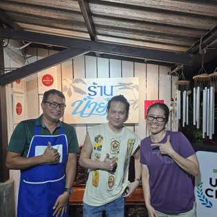 Three staff giving thumbs up in front of the Naam Yoi shop sign at night, Southern Thai restaurant in Phuket Old Town