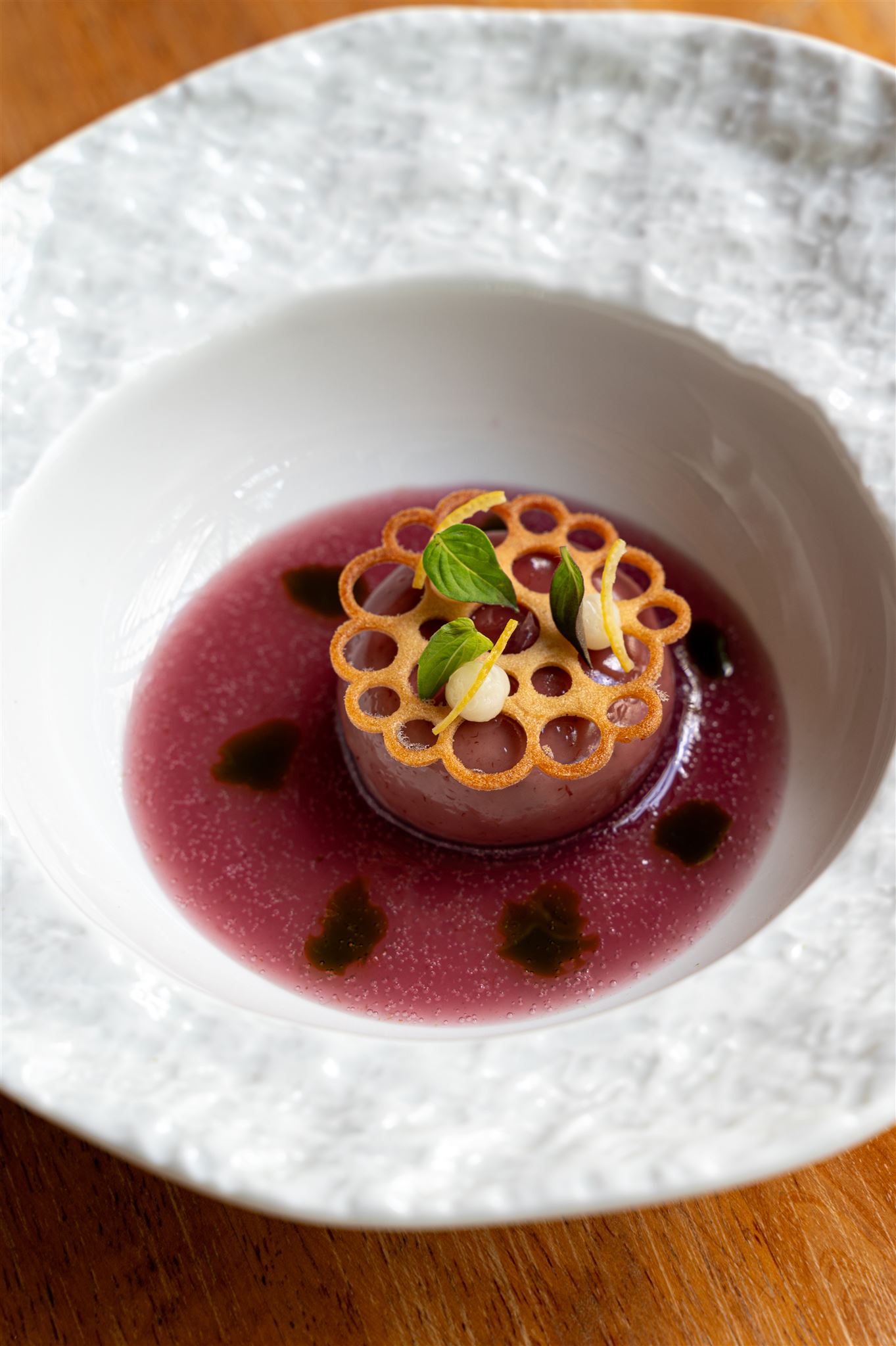 Fine dining dish of purple set custard in magenta broth with lacy tuile and herbs at Nitan Southern Thai restaurant, Bang Tao, Phuket