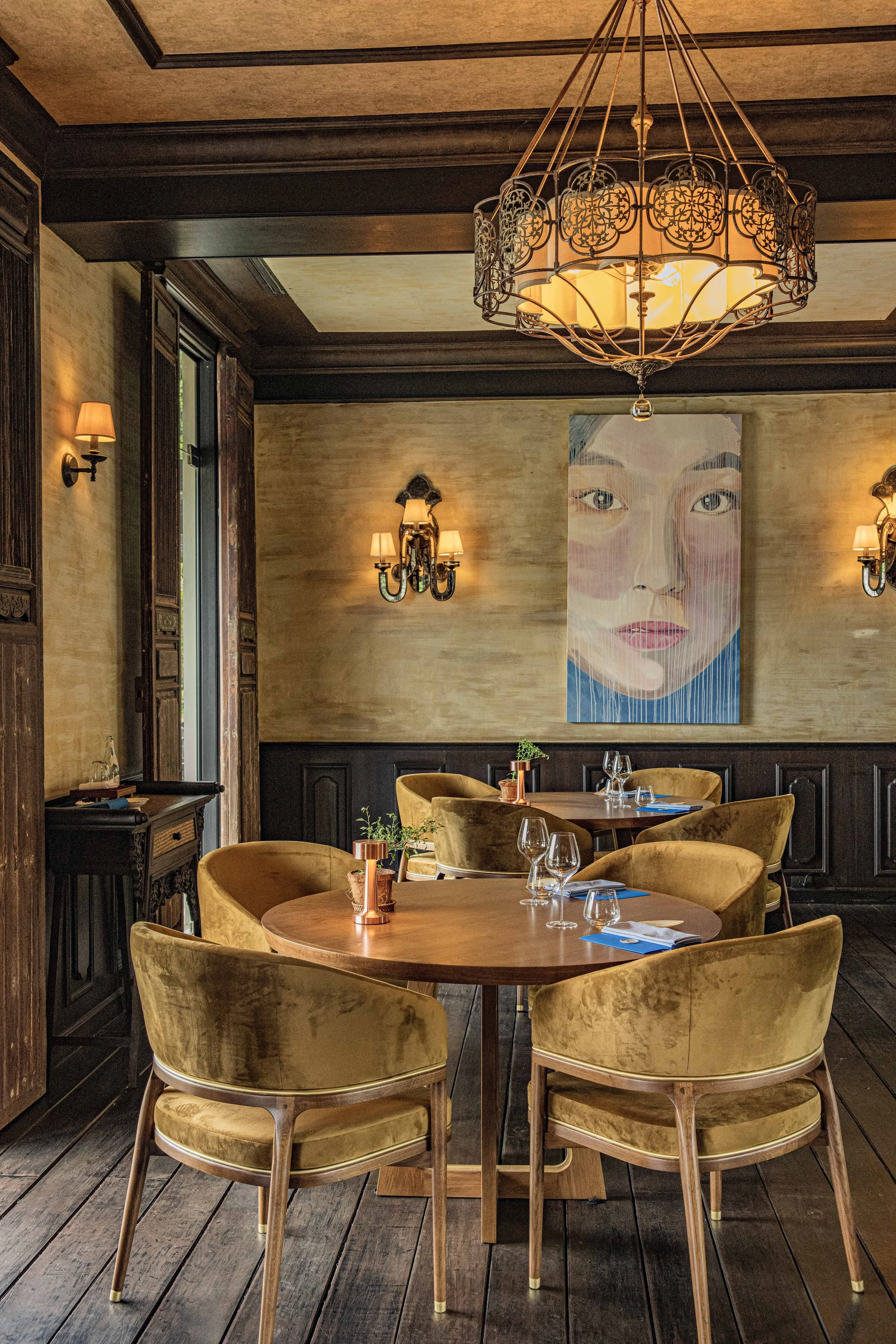 Antique-filled dining room at Samut with dark teak wood, velvet chairs and a portrait painting, a Southern Thai restaurant in Rawai, Phuket.