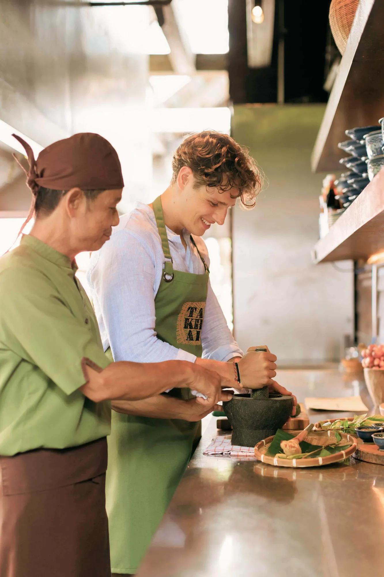 Chef teaching a guest to pound ingredients with a mortar and pestle at Ta Khai Thai restaurant, Rosewood Phuket in Patong
