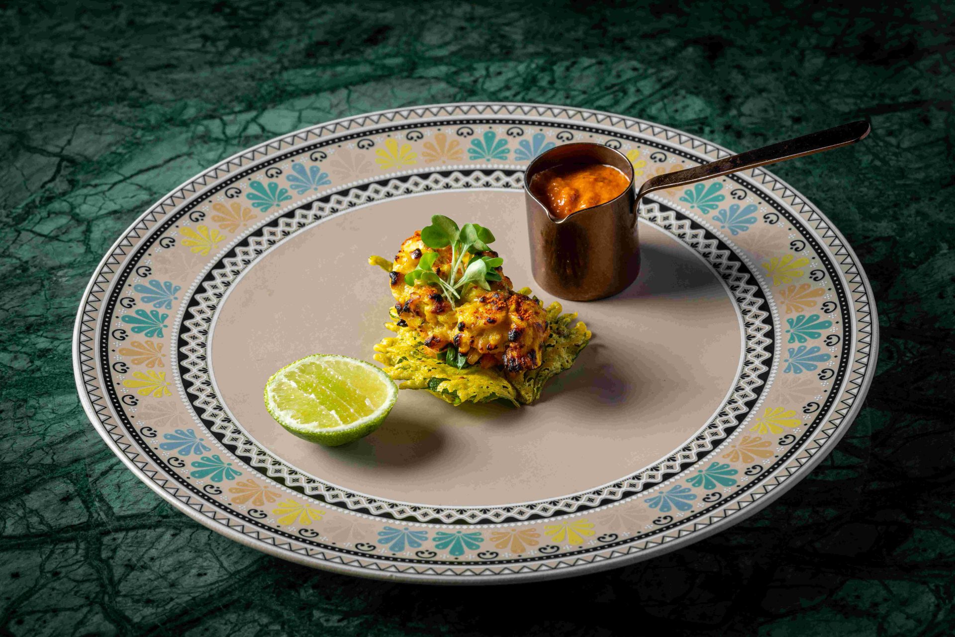 Chargrilled chicken tikka with lime, microgreens and a copper pot of sauce on an ornate plate at Tambu, an Indian restaurant in Patong, Phuket