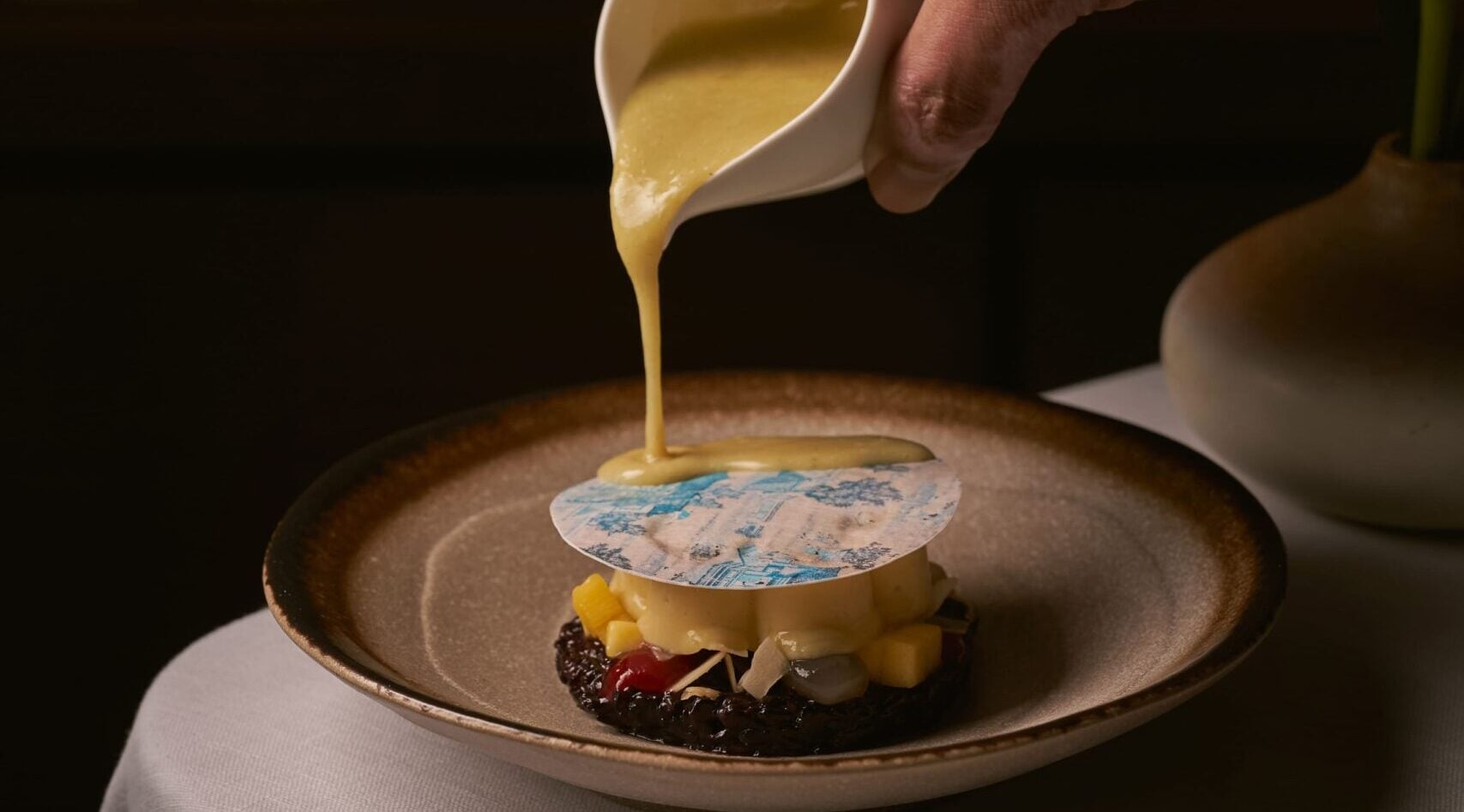 Chef pouring yellow sauce over a black rice dish with decorative wafer at Thai Library, a fine-dining Thai restaurant in Bang Tao, Phuket